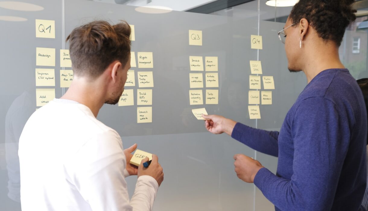 Two people mapping a process with sticky notes on a glass wall
