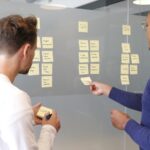Two people mapping a process with sticky notes on a glass wall